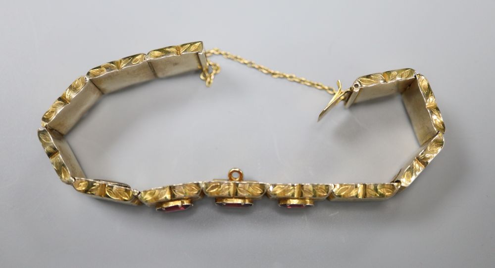 A Victorian engraved yellow metal and three stone garnet set hinged panel bracelet, with safety chain, gross 21.7 grams.